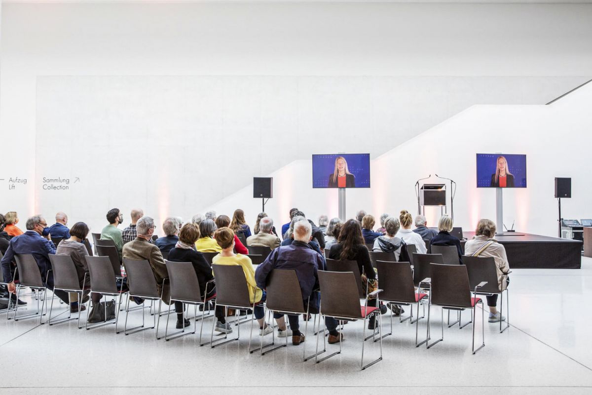 Eine Gruppe Menschen sitzt in einem Museum und hört einem Vortrag zu